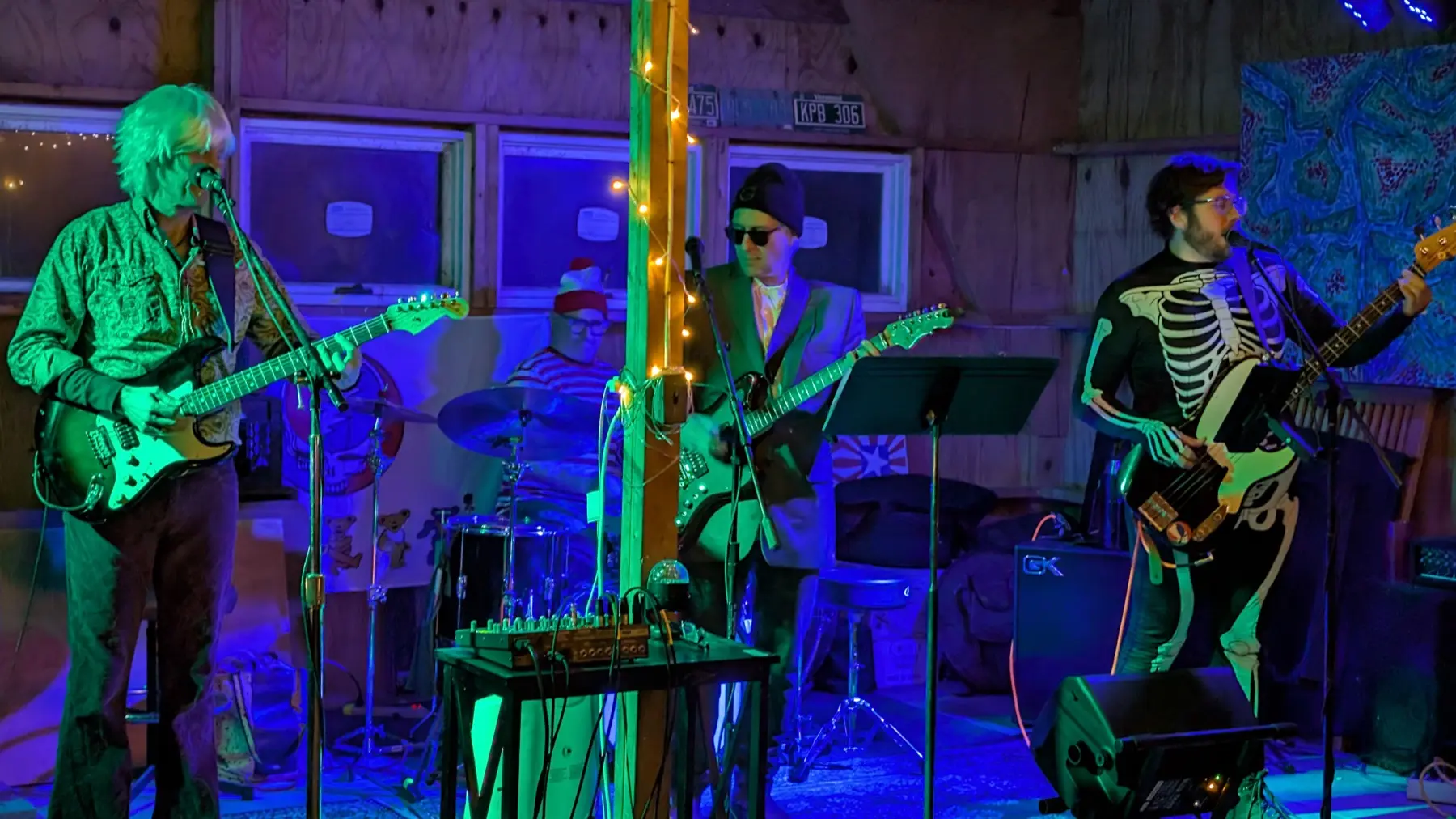 Four of the band mid-song in Halloween costume, under blue and green stage light