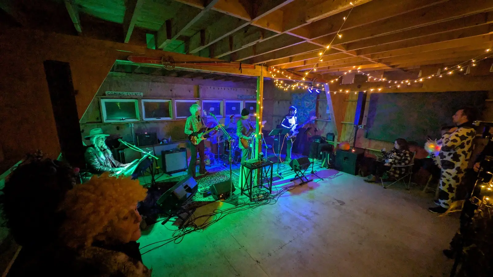 The whole band playing in the barn under string lights, with a small audience in costume watching